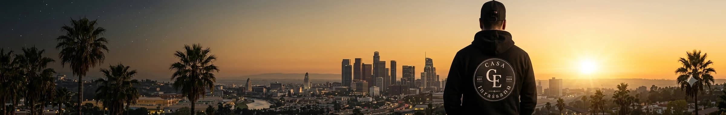 Man in a Casa Empresario hoodie looking out over a city skyline at sunset