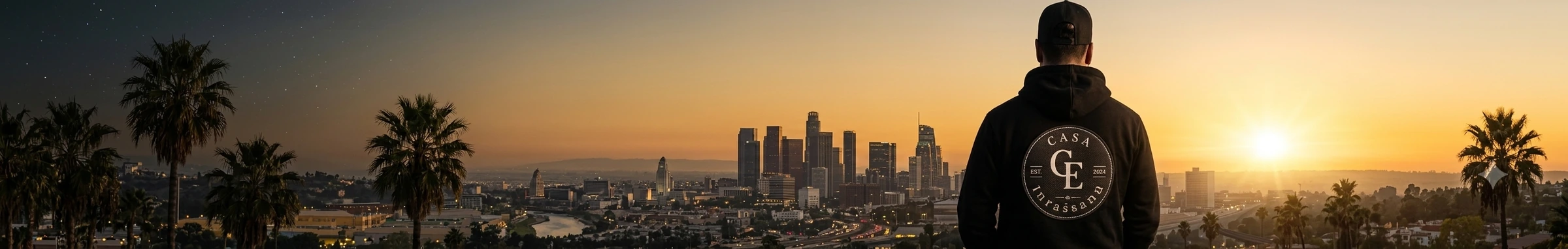 Man in a Casa Empresario hoodie looking out over a city skyline at sunset